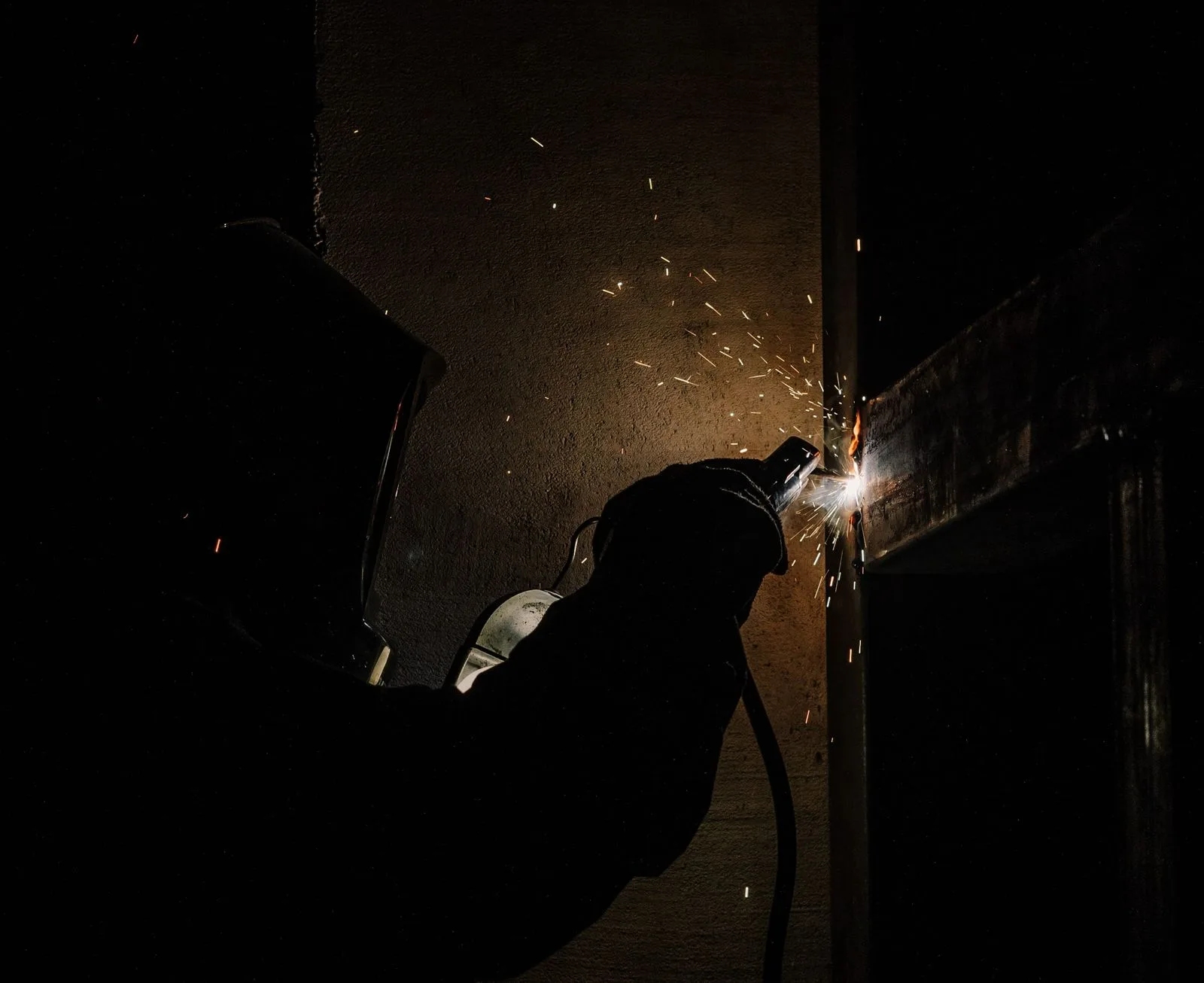 Welder working in a dark workshop, sparks flying off a steel frame